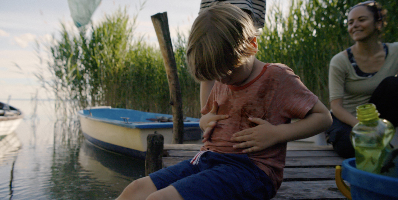 Liten pojke satt vid en sjö och fick sin t-shirt smutsig