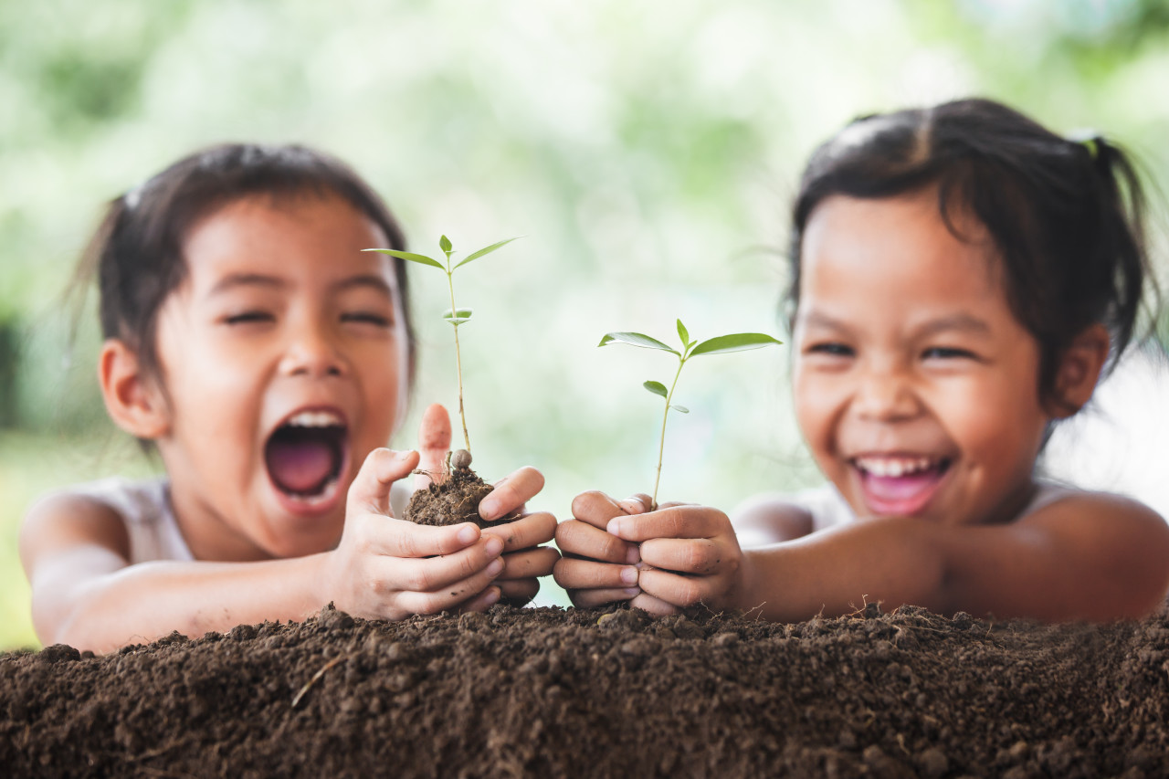Två barn leende mot en växt som växer
